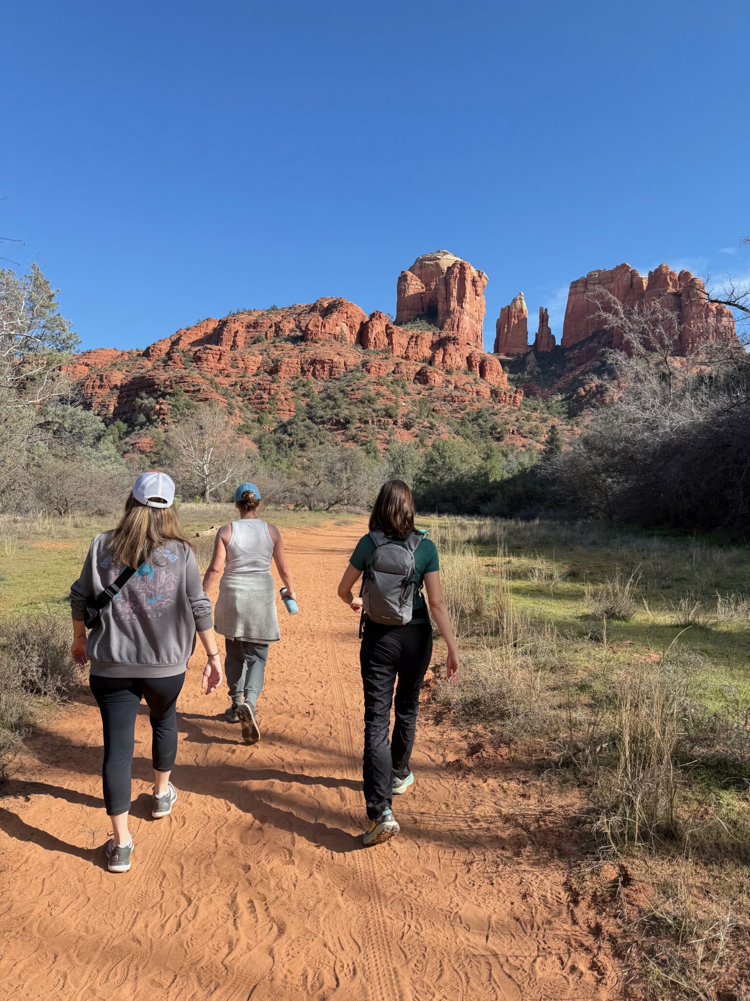 Three women hiking a red dirt trail toward Cathedral Rock in Sedona